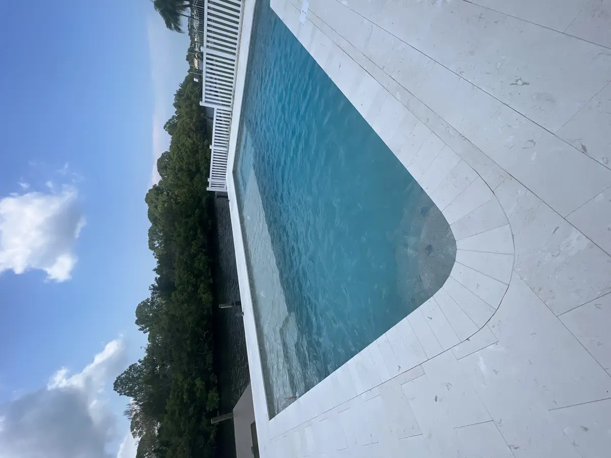 Finished rectangular concrete pool next to a waterway canal with travertine decking