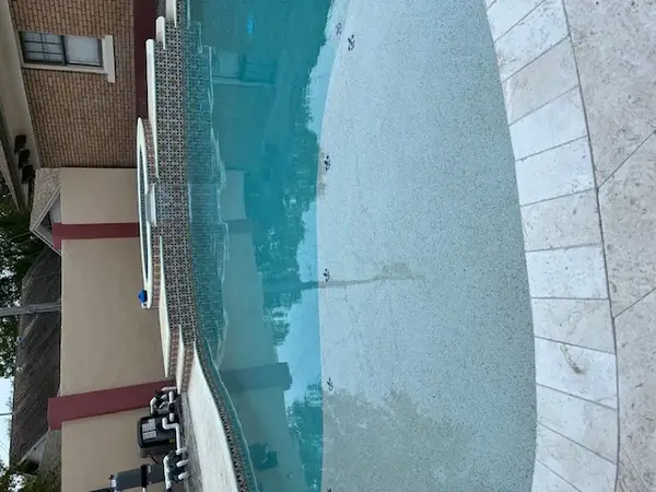 Curved residential pool with raised spa, travertine pavers, and clean equipment set