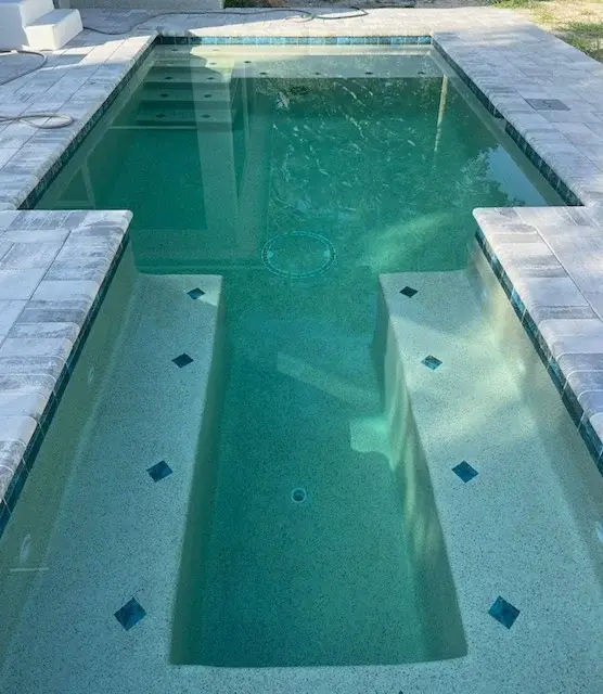 Completed geometric concrete pool featuring double tanning shelves and grey pavers