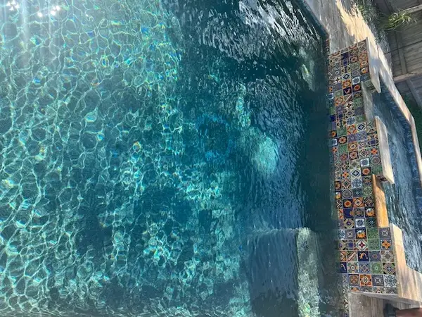 Custom hand-painted Mexican Talavera tiles lining the raised wall of a teal-water pool